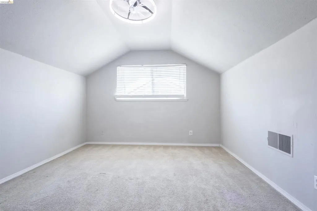 Vaulted ceiling room featuring light gray walls, carpet flooring, a window with blinds, and a built-in ceiling light fixture