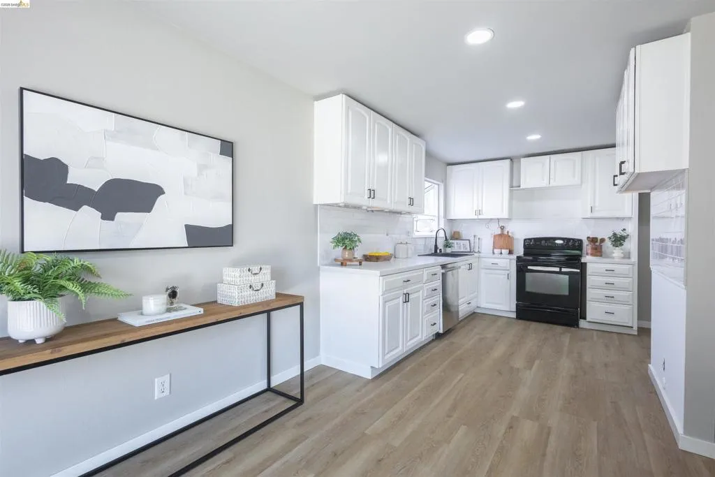 Modern kitchen featuring white cabinetry, light countertops, wood-finish flooring, a black range, and recessed lighting