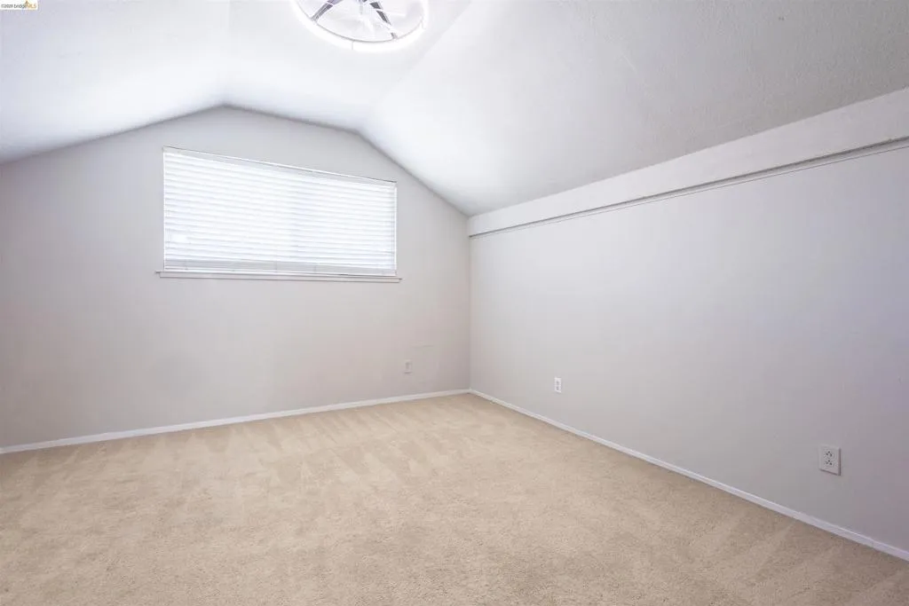 Room featuring sloped ceilings, beige carpet flooring, a horizontal window with blinds, and a built-in ceiling light fixture