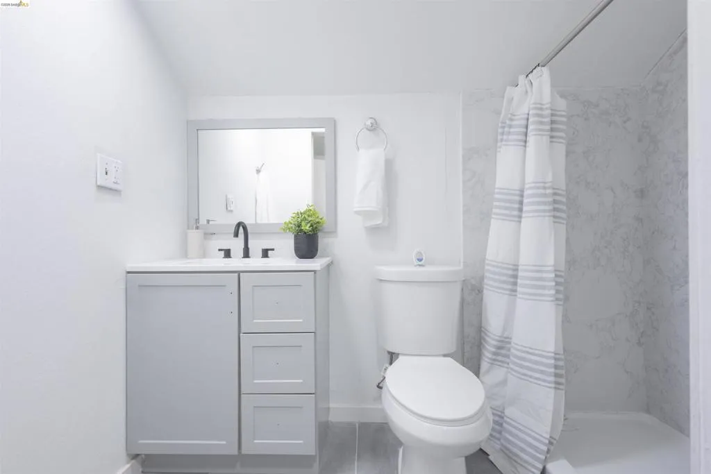 Contemporary bathroom featuring a light gray vanity with white countertop, matte black faucet, and a shower with marble-look wall panels