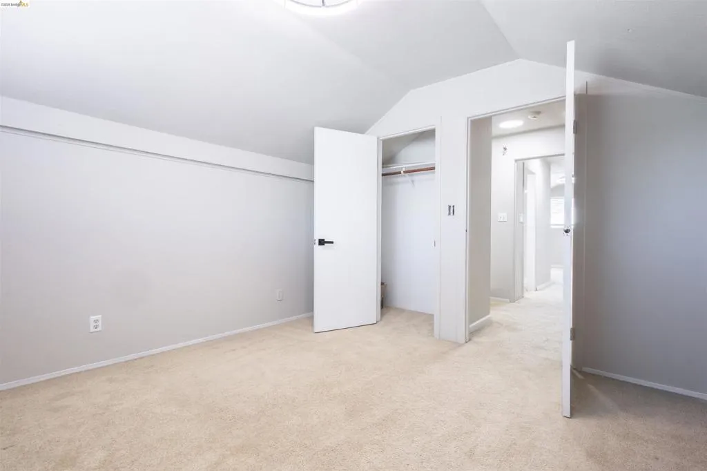 Carpeted room featuring a vaulted ceiling and a built-in closet with shelving and hanging rod