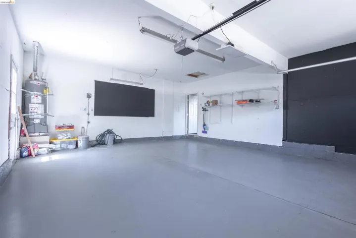 Spacious garage with light gray finished flooring, white painted walls, exposed ceiling joists, and track lighting