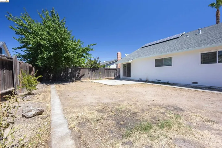 Spacious rear yard with a concrete patio, wood fencing, mature tree, and solar panels on the roofline