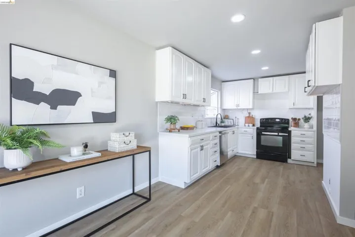 Modern kitchen featuring white cabinetry, light countertops, wood-finish flooring, a black range, and recessed lighting