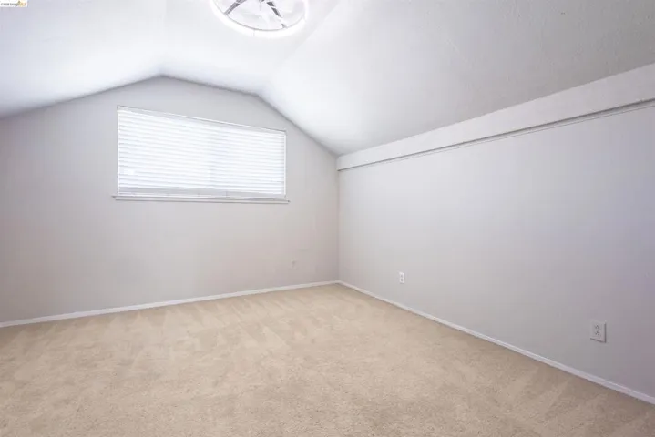 Room featuring sloped ceilings, beige carpet flooring, a horizontal window with blinds, and a built-in ceiling light fixture