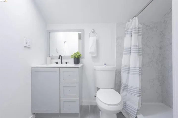 Contemporary bathroom featuring a light gray vanity with white countertop, matte black faucet, and a shower with marble-look wall panels