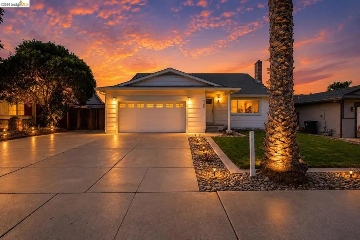 White exterior residence featuring an attached garage, concrete driveway, and front yard landscaping with decorative rock beds