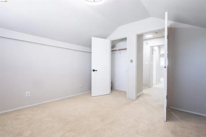 Carpeted room featuring a vaulted ceiling and a built-in closet with shelving and hanging rod