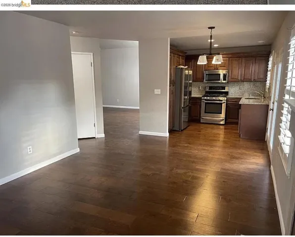 Open-concept kitchen featuring wood-finish cabinetry, stainless steel appliances, a tiled backsplash, and granite-style countertops