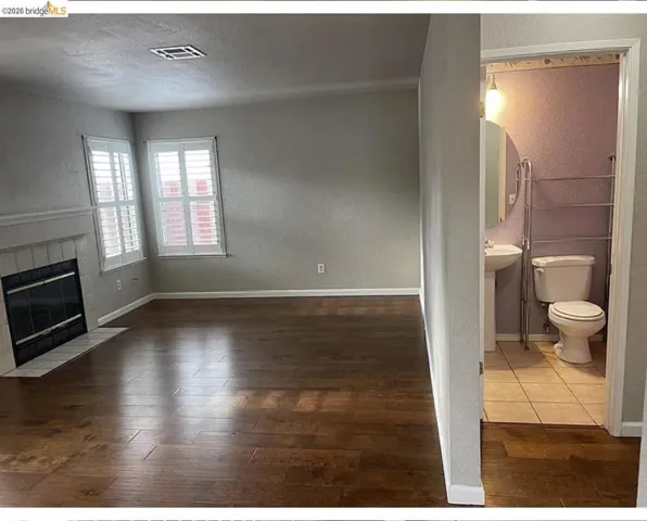 Spacious living area featuring wood-finish flooring, a fireplace with a tiled hearth, and windows with plantation shutters