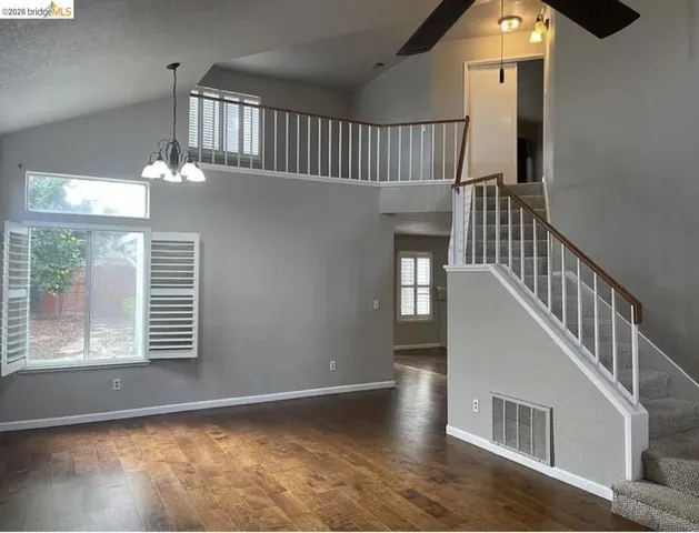 Spacious living area featuring high vaulted ceilings, wood-finish flooring, and a second-story overlook with a white railing