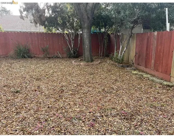 Private backyard area featuring a red-stained perimeter fence, mature trees, and a ground cover of leaves