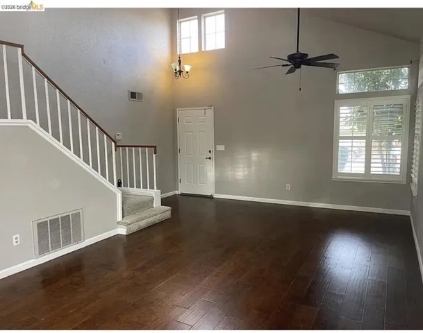 Vaulted ceiling living area featuring rich wood-finish flooring, a contemporary ceiling fan, and white plantation shutters