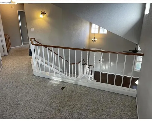 Carpeted upper landing with a white painted stair railing and wood-tone handrail overlooking a lower level with wood-finish flooring