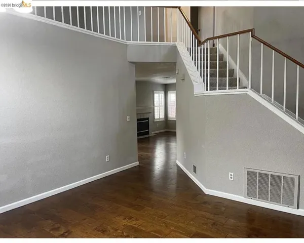 Foyer featuring wood-finish flooring, a carpeted staircase with white balusters and wood handrails, and a view into a living space with a fireplace and windows
