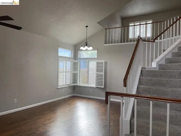 Open-concept interior featuring wood-finish flooring, vaulted ceilings, and a carpeted staircase with wood handrails