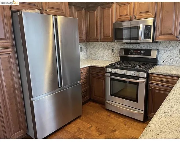 Kitchen featuring rich wood cabinetry, stone countertops, stainless steel appliances, and wood-finish flooring