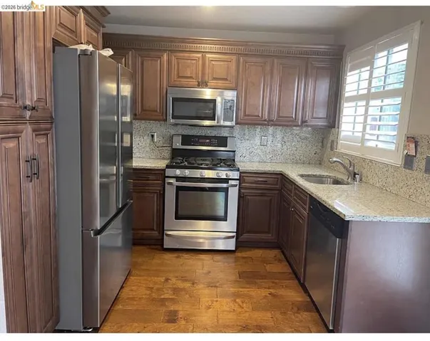 U-shaped kitchen featuring wood-finish cabinetry, granite countertops with matching backsplash, stainless steel appliances, and wood-finish flooring