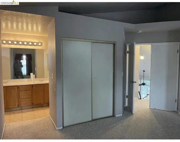 Bedroom area featuring neutral carpeting, a double-door closet, and an entry to a bathroom with a dual-sink vanity