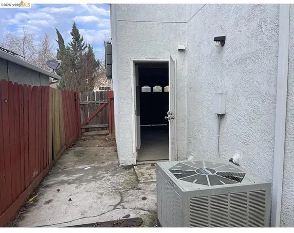 Exterior stucco finish with an access door, concrete pathway, and a red-stained wooden fence
