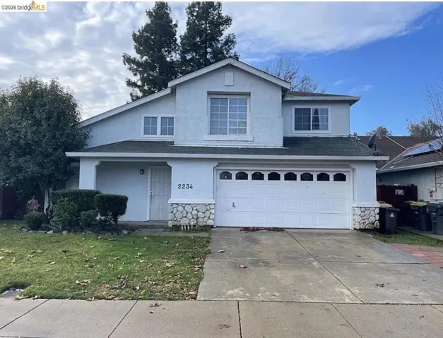 Two-story stucco exterior featuring a covered entry, stone accents, and a two-car garage with arched window inserts