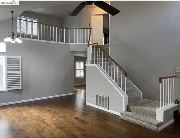 Open-concept living area featuring wood-finish flooring, a two-story ceiling, and a carpeted staircase with a white baluster railing and wood handrail