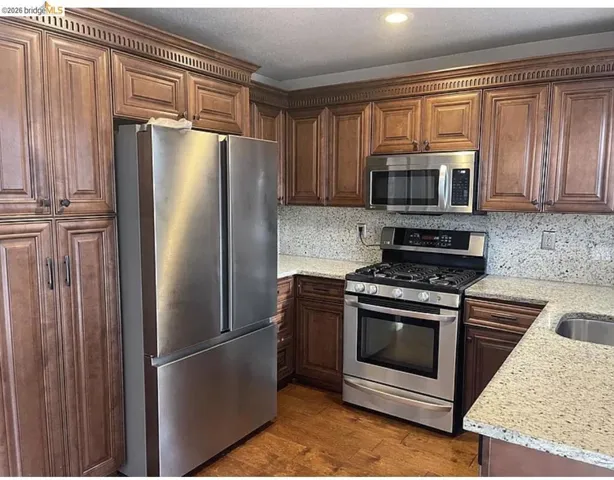 Kitchen featuring dark wood cabinetry with crown molding, stainless steel appliances, granite countertops, and wood-finish flooring