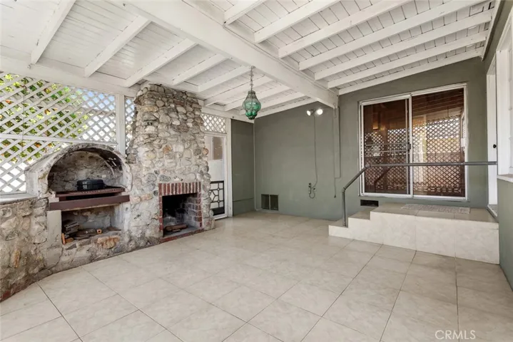 Lattice-enclosed covered patio with tile flooring, stone fireplace and wood-fired oven.