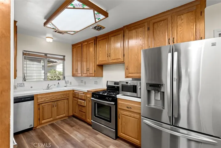 Kitchen with tile counters, stainless appliances, and wood-vinyl flooring.
