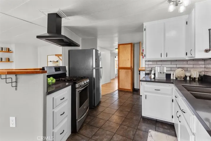 Clean and functional kitchen featuring bright white cabinetry, dark countertops, a classic tile backsplash, gas range with modern hood, ample cabinet storage, and an open flow to the living areas.