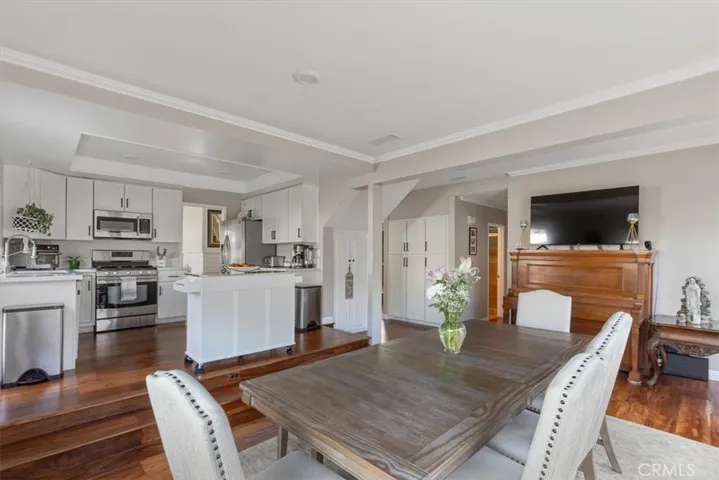 Formal dining area with elegant crown molding, rich wood flooring, and an open layout that flows seamlessly into the kitchen