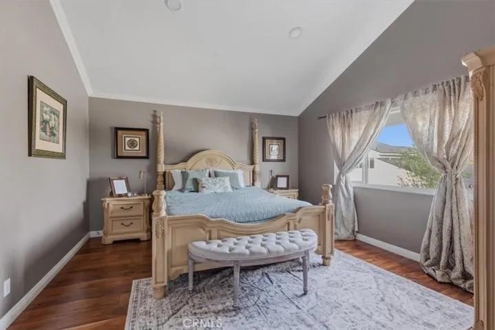 Spacious primary bedroom with vaulted ceilings, rich hardwood flooring, and a large picture window that fills the room with natural light.