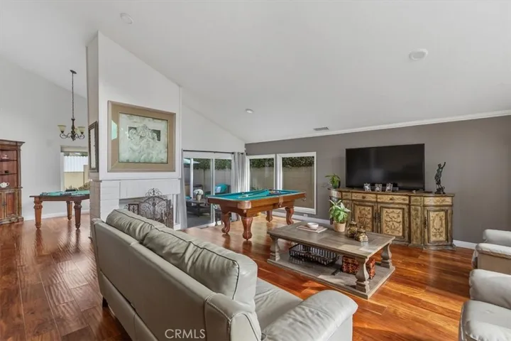 Spacious living room with vaulted ceilings, recessed lighting, rich hardwood flooring, and a cozy fireplace. Sliding glass doors provide seamless access to the private patio, creating an ideal indoor-outdoor living experience.