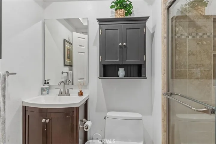 Updated bathroom featuring a modern vanity, framed mirror, tiled walk-in shower with glass enclosure, and convenient built-in storage cabinet.