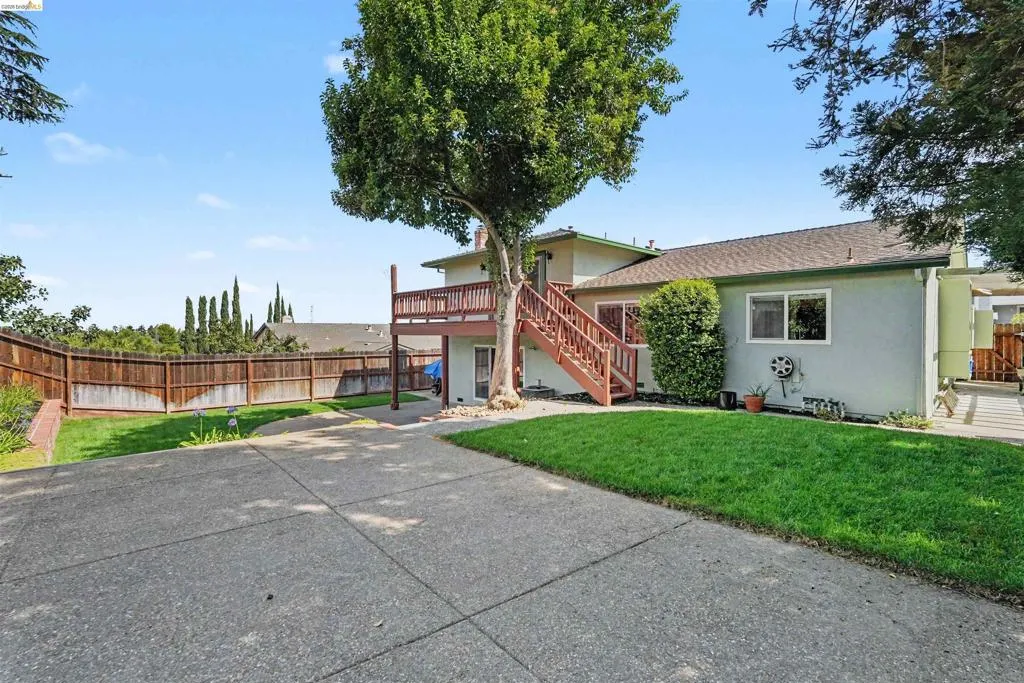 Expansive concrete driveway, terraced yard with a wood fence, and a multi-level deck with wood railing