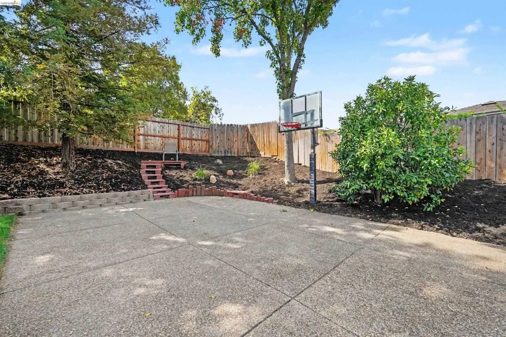 Expansive concrete patio with a retaining wall, terraced landscaping, and a wood privacy fence