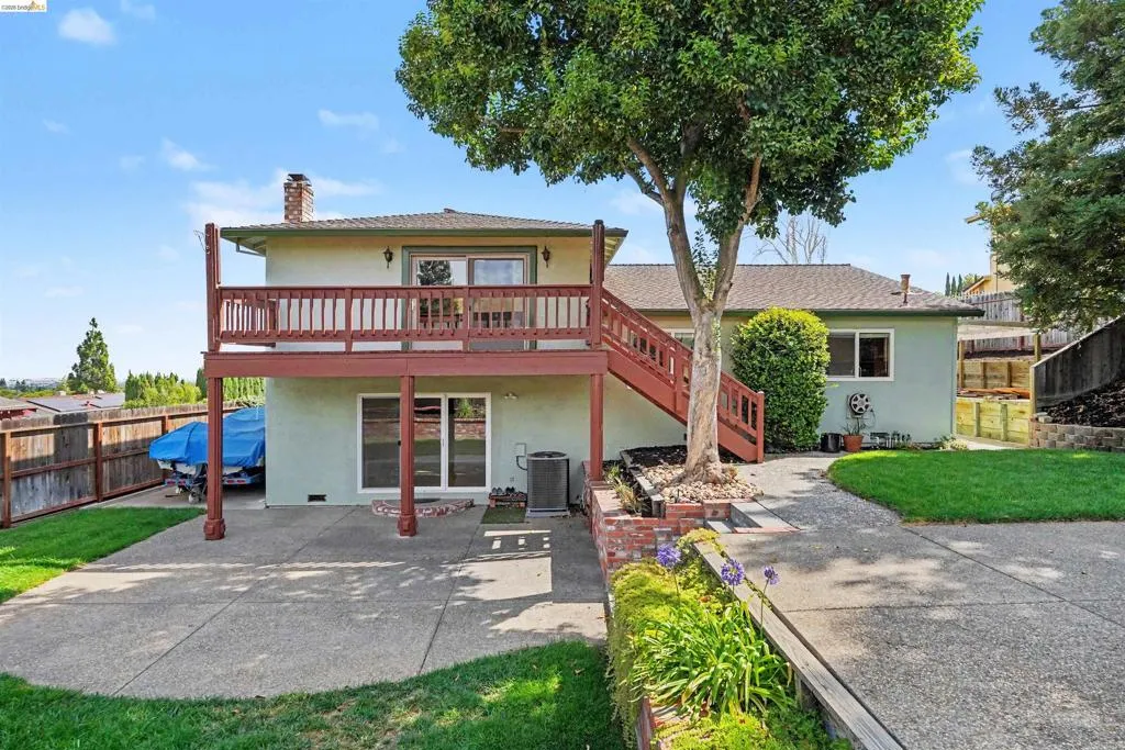 Multi-level rear exterior with a second-story deck, ground-level patio, and a tiered landscaped yard with mature trees