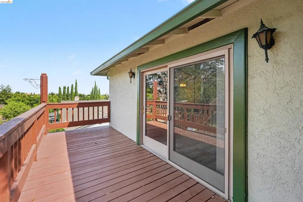 Expansive outdoor deck with wood-finish railing, a stucco exterior, and double sliding glass doors