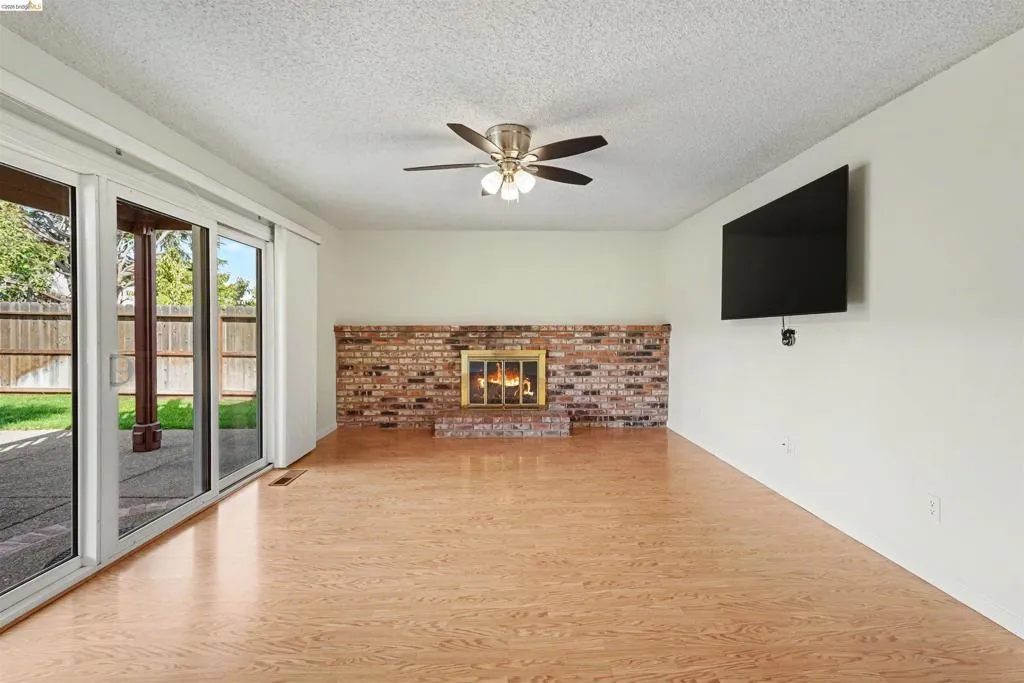 Wood-finish flooring, brick fireplace surround, ceiling fan with light fixture, and sliding glass door