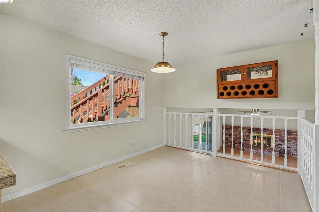 Tile flooring, built-in wooden wine rack with glass-front cabinetry, window with white trim, brass-finish pendant light fixture, and white painted railing