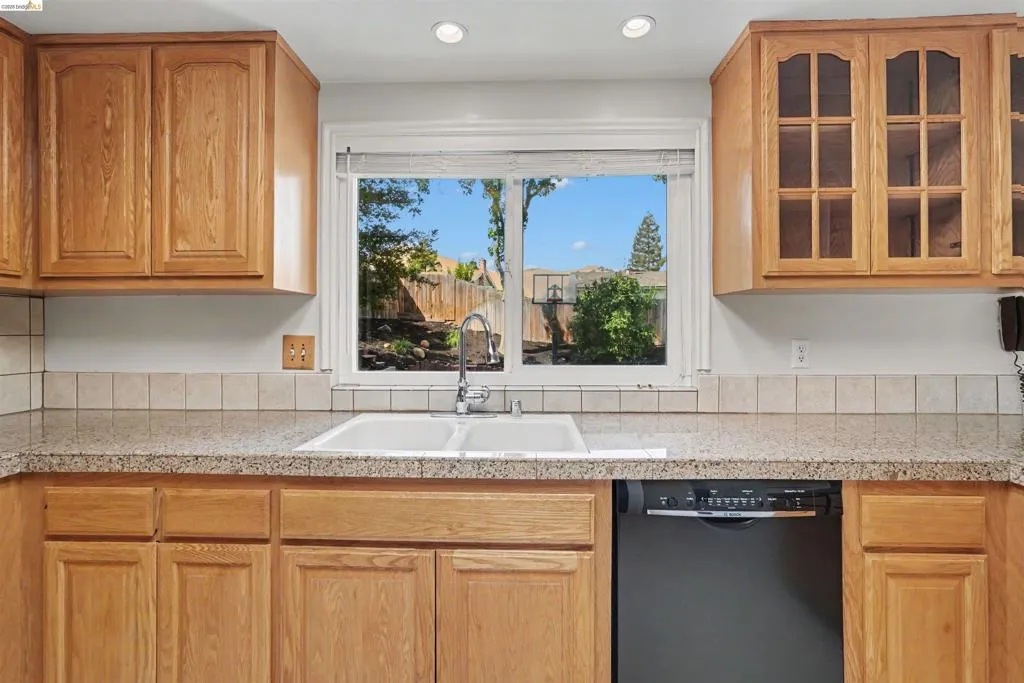 Wood-finish cabinetry, recessed lighting, tile backsplash, laminate countertops, and a dual basin sink with a single-handle faucet