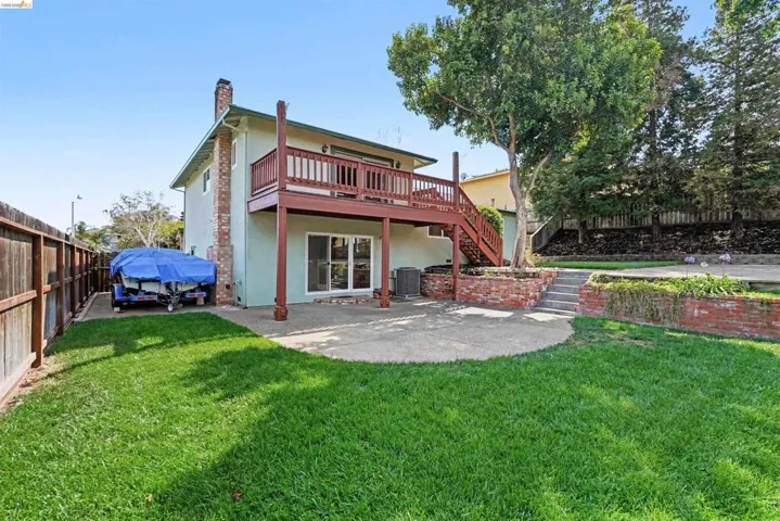 Expansive backyard featuring a concrete patio, a raised wood deck with balusters, and brick retaining walls