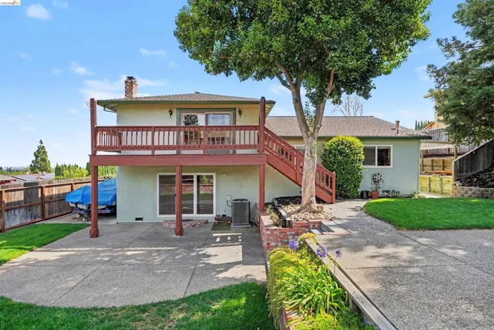 Multi-level rear exterior with a second-story deck, ground-level patio, and a tiered landscaped yard with mature trees