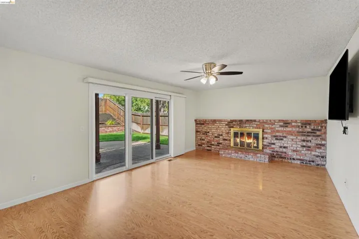 Wood-finish flooring, brick fireplace with a brass firebox, ceiling fan with integrated lighting, and sliding glass doors to the exterior