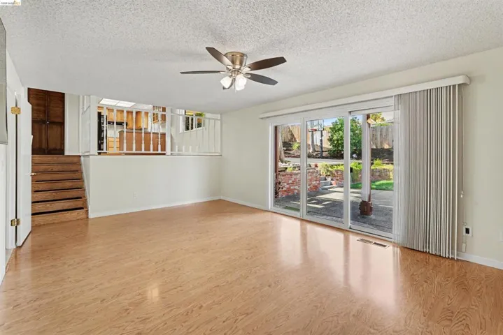 Wood-finish flooring, ceiling fan with integrated lighting, and a sliding glass door with vertical blinds