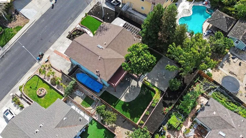 Paved driveway, covered pool, pergola-covered patio, mature trees, and landscaped yard