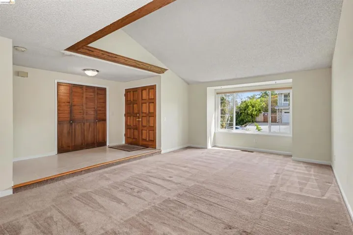 Entryway featuring a wood-panel door and bifold closet doors, with a vaulted ceiling and exposed wood beam