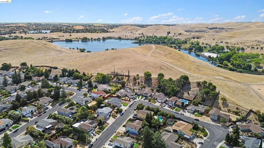 Residential neighborhood with mature trees, surrounded by rolling hills and a visible body of water
