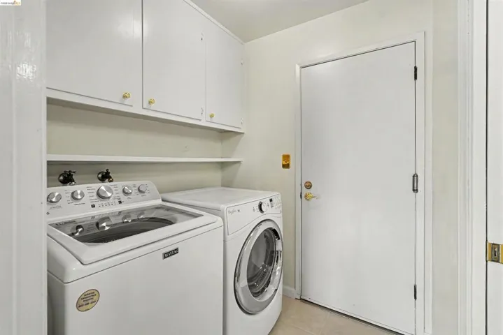 Laundry area with upper cabinetry and open shelving, featuring tile flooring
