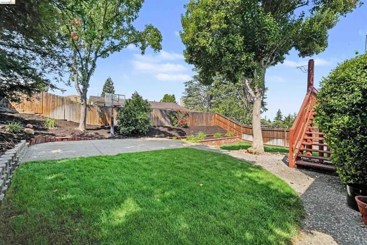 Expansive backyard featuring a manicured lawn, concrete patio, and sloped landscaping with mature trees